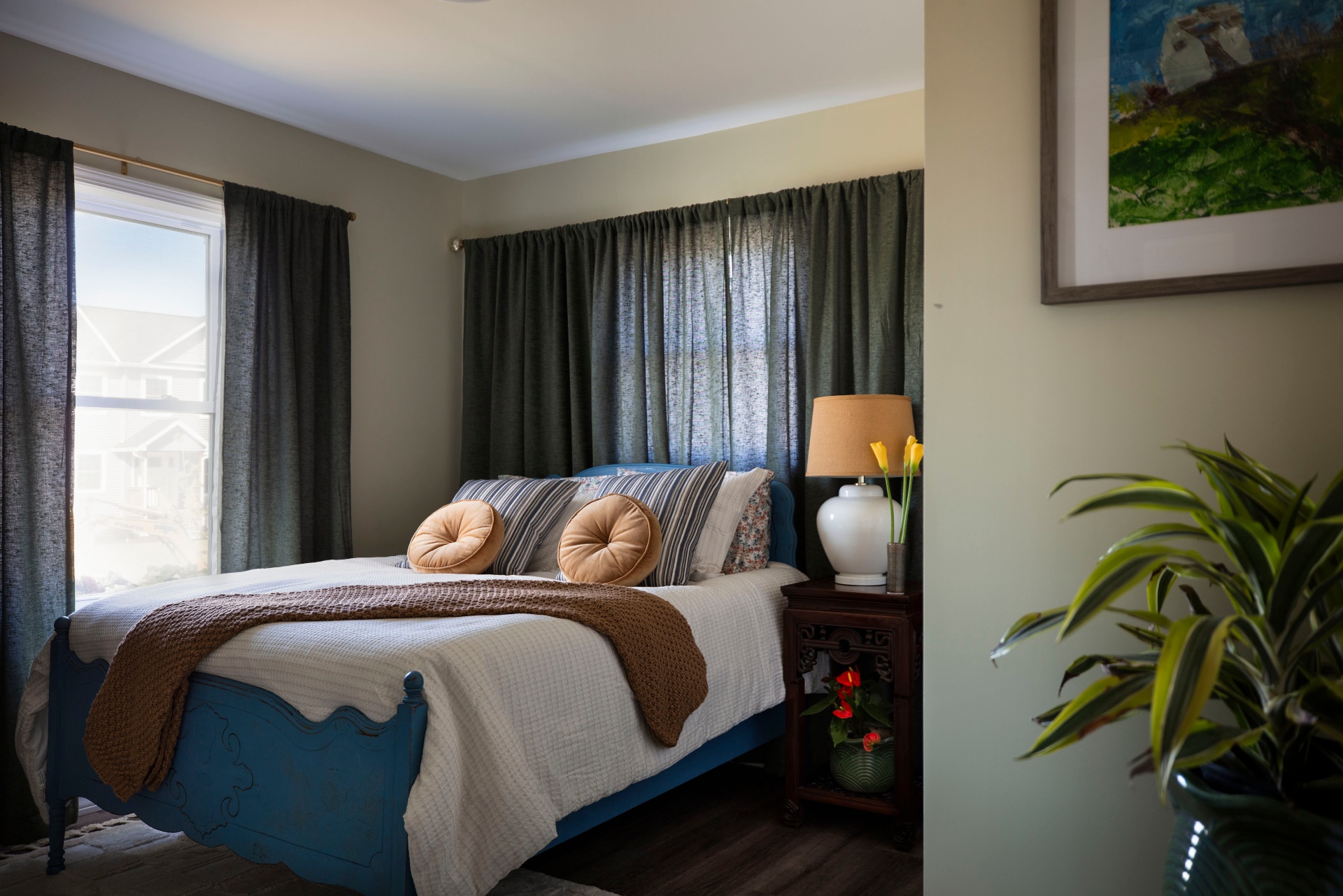 Finished showhouse bedroom with blue carved bed frame, layered linens and moody green drapery