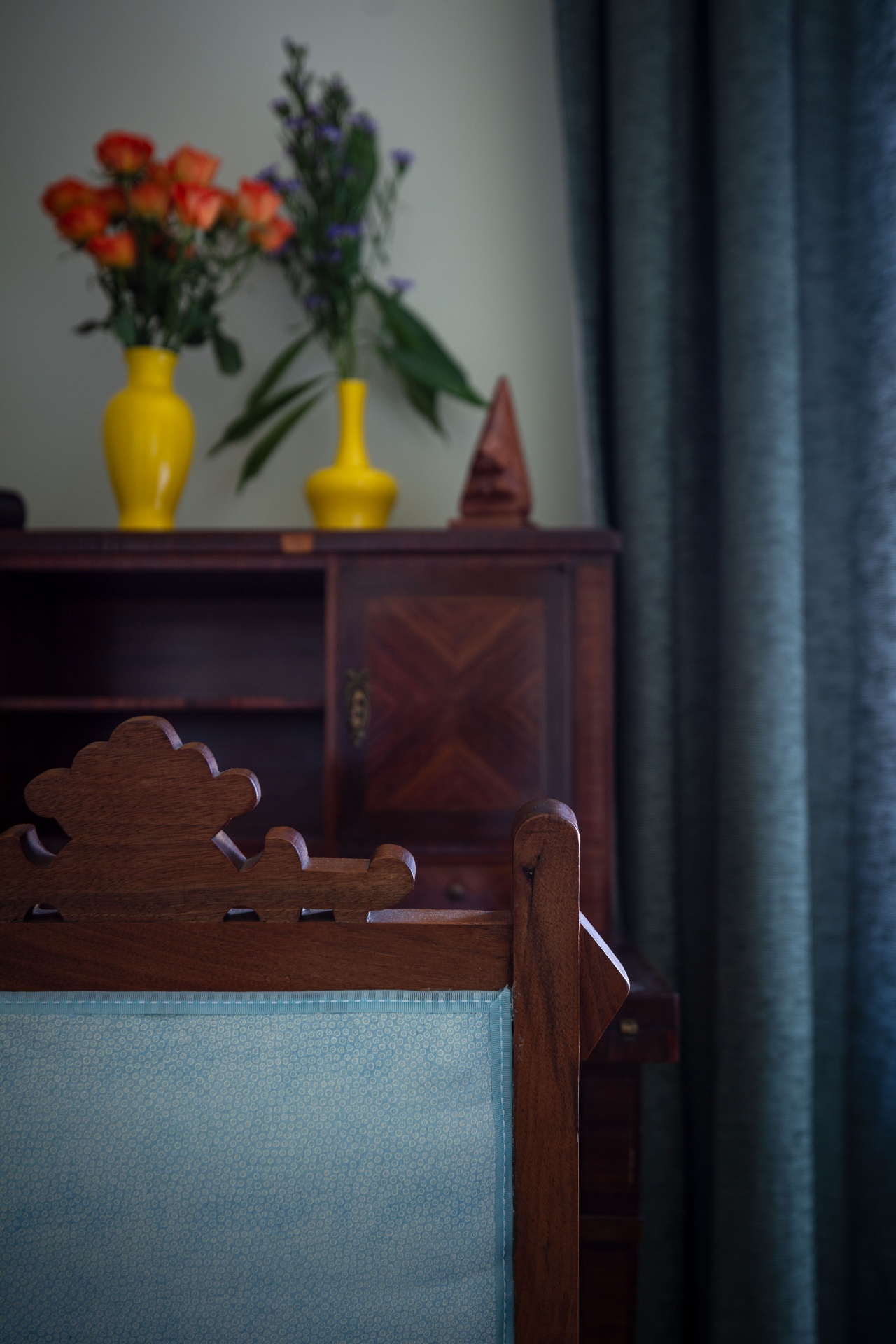 Detail of antique wooden secretary desk with yellow vases and a curved-back upholstered chair