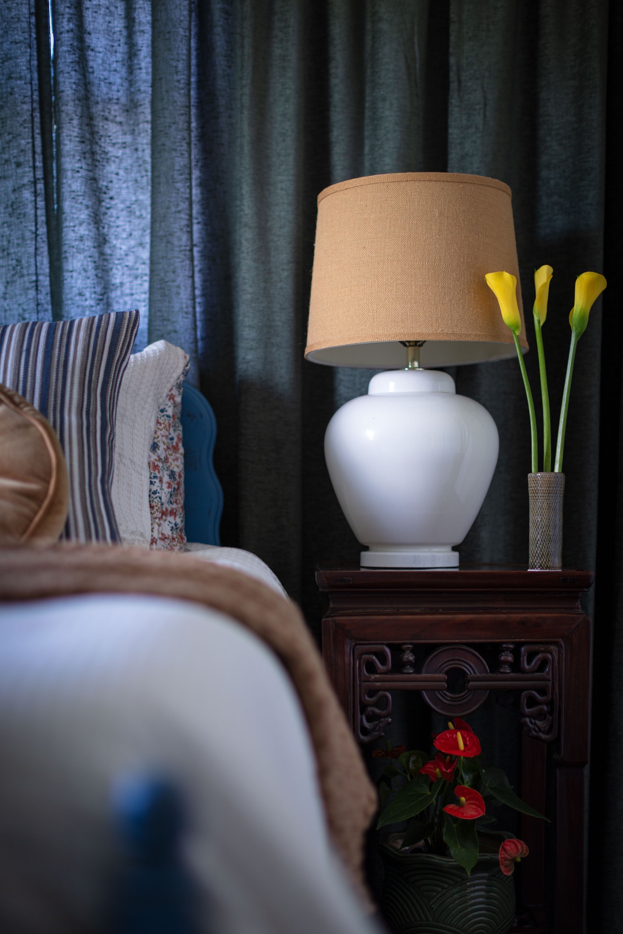 Bedside view with carved side table, ginger jar lamp, and layered striped and floral pillows
