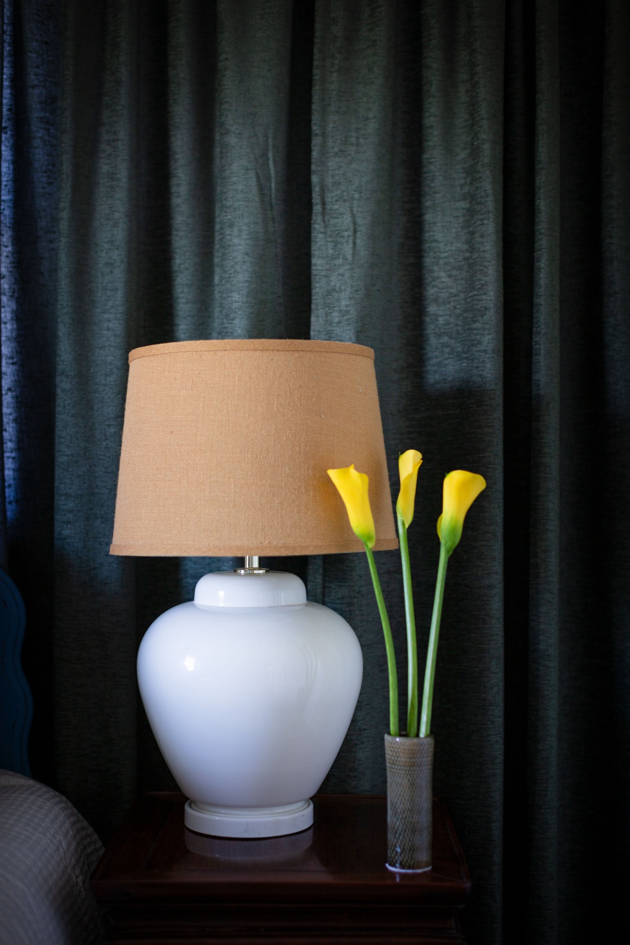White ceramic ginger jar lamp with burlap shade and yellow calla lilies against green drapery