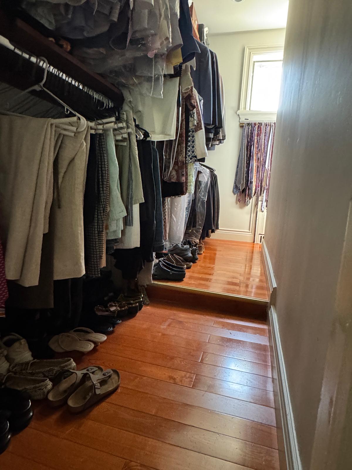 Existing narrow walk-in closet packed with clothing and shoes